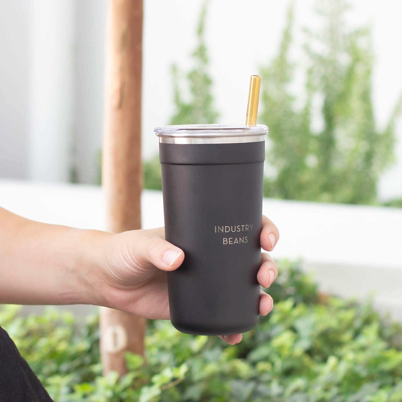Person holding a black insulated tumbler with a straw outdoors