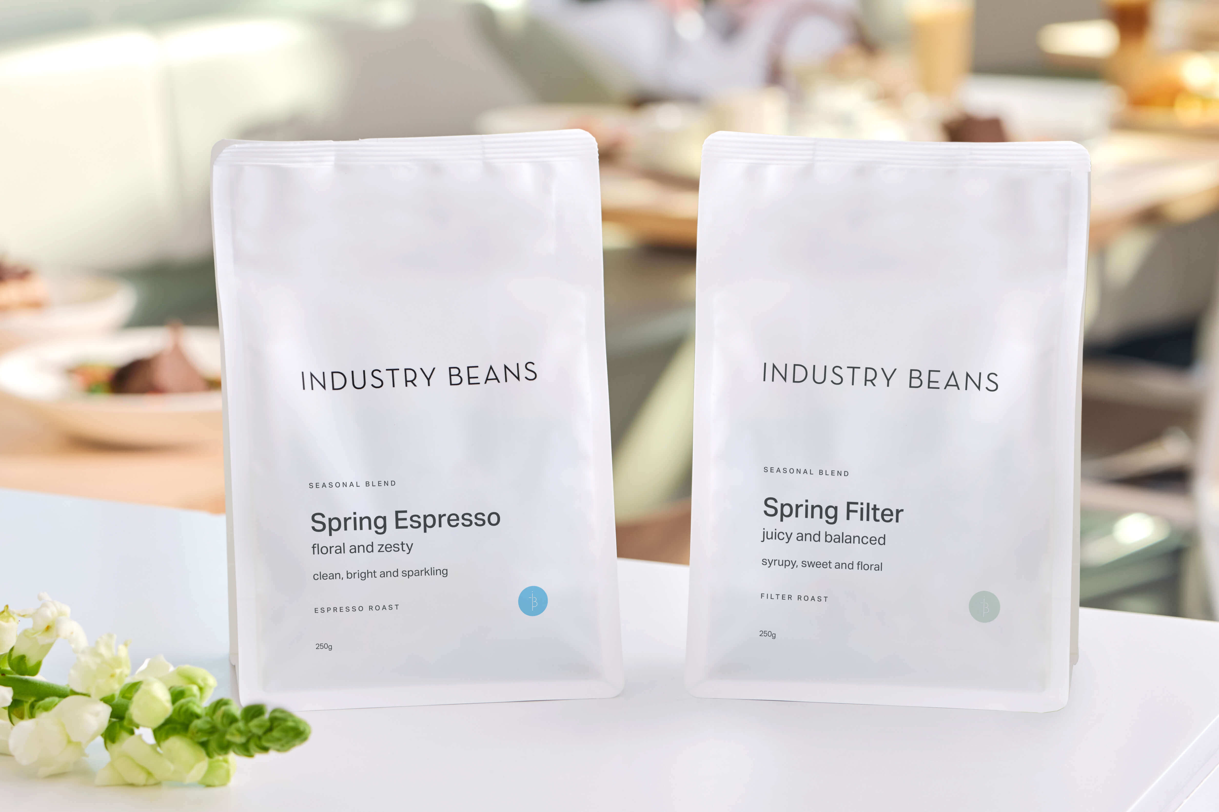 Two bags of 'Industry Beans' coffee on a table with a blurred background