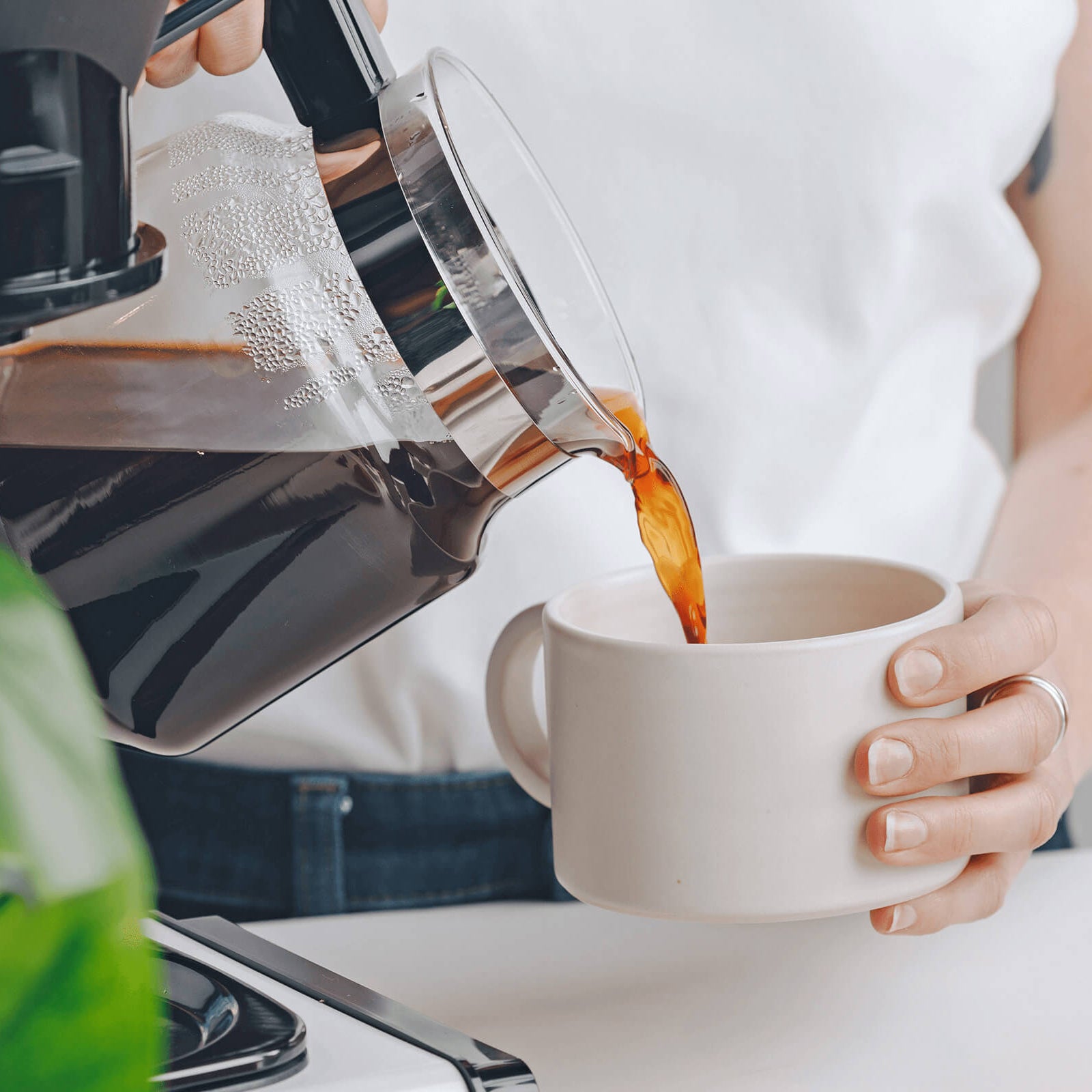 Person pouring coffee from a Moccamaster into a white mug.
