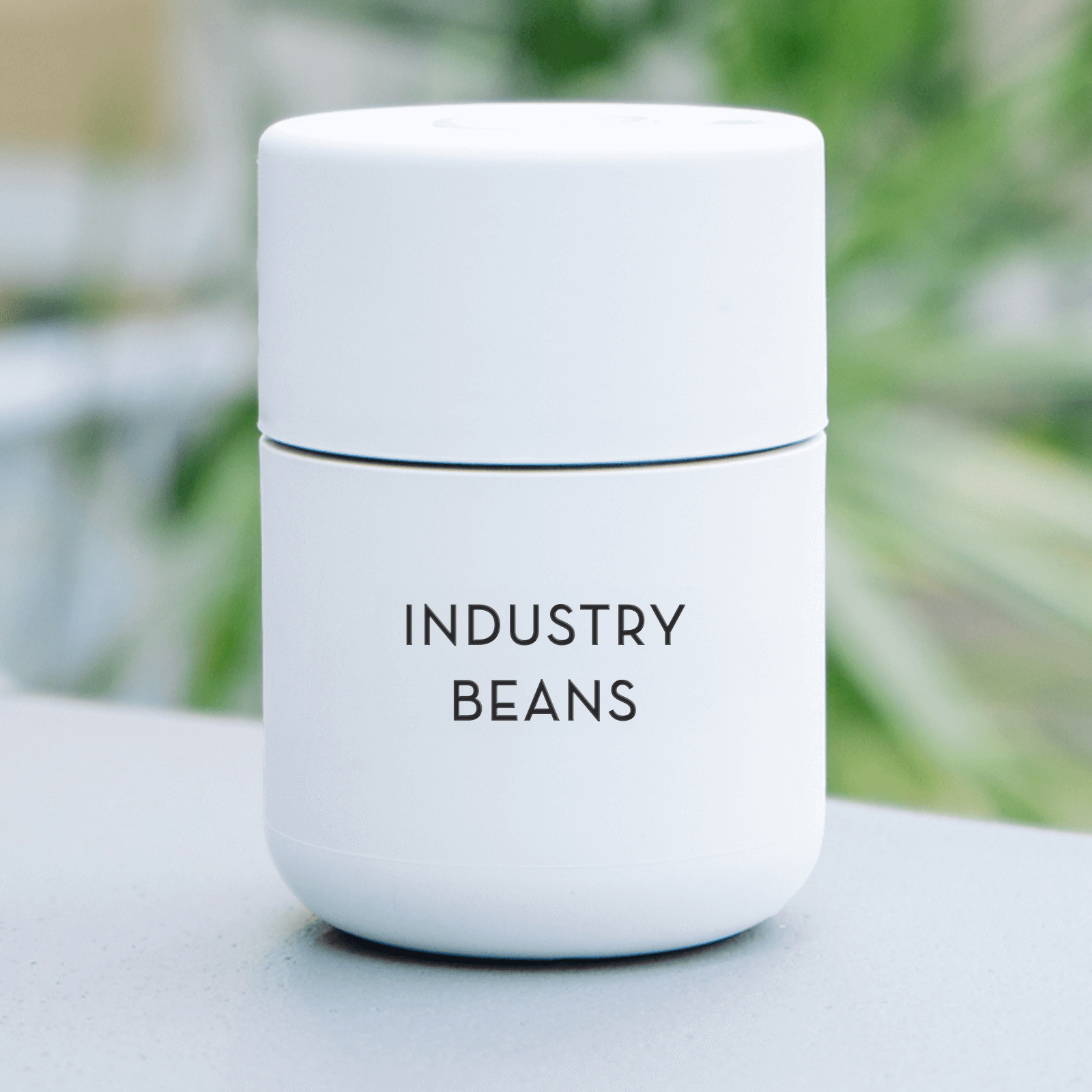 White cup labeled 'Industry Beans' on a blurred natural background