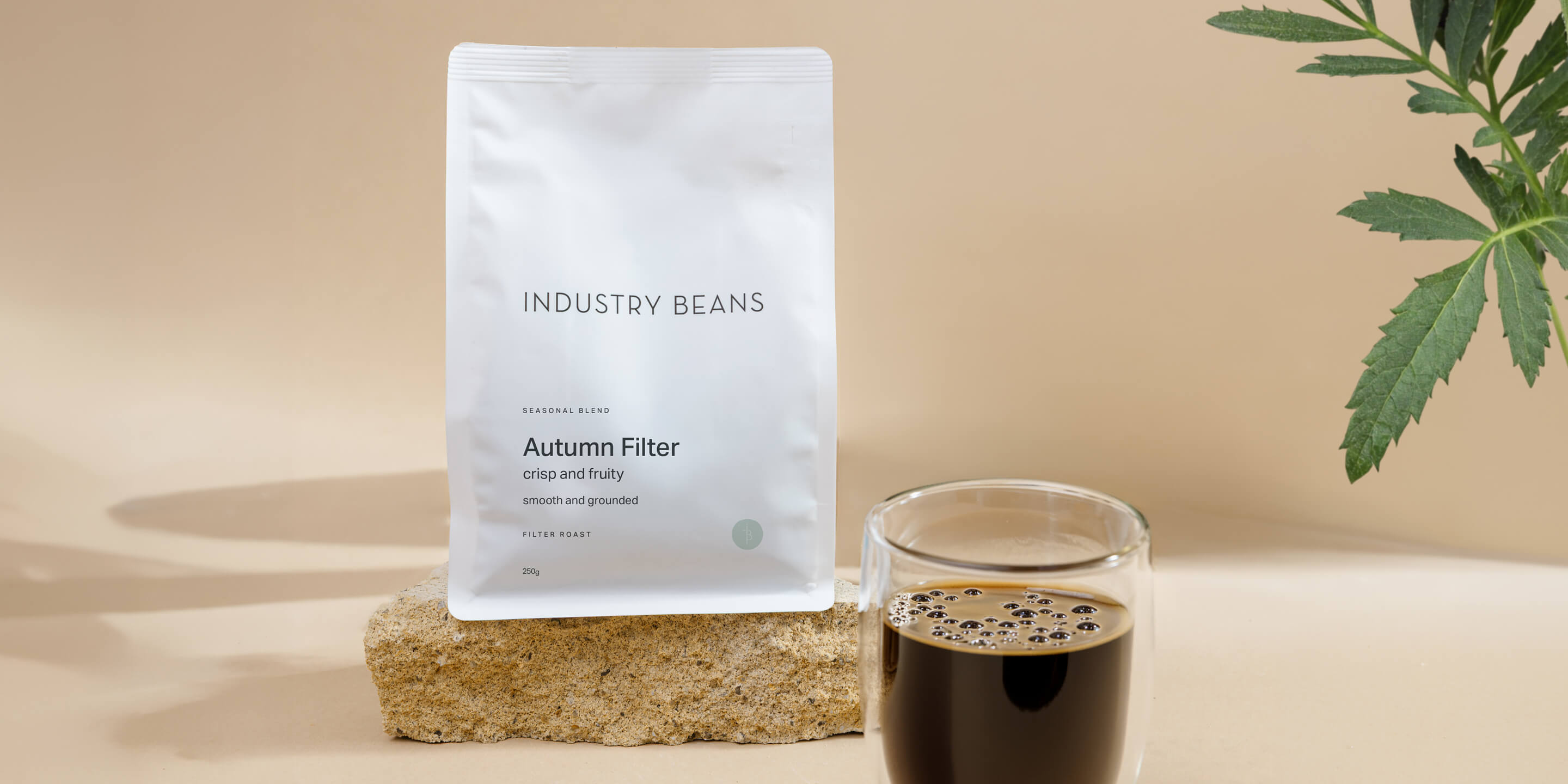 Bag of Industry Beans Autumn Filter Blend on sandstone block with glass mug of filter coffee
