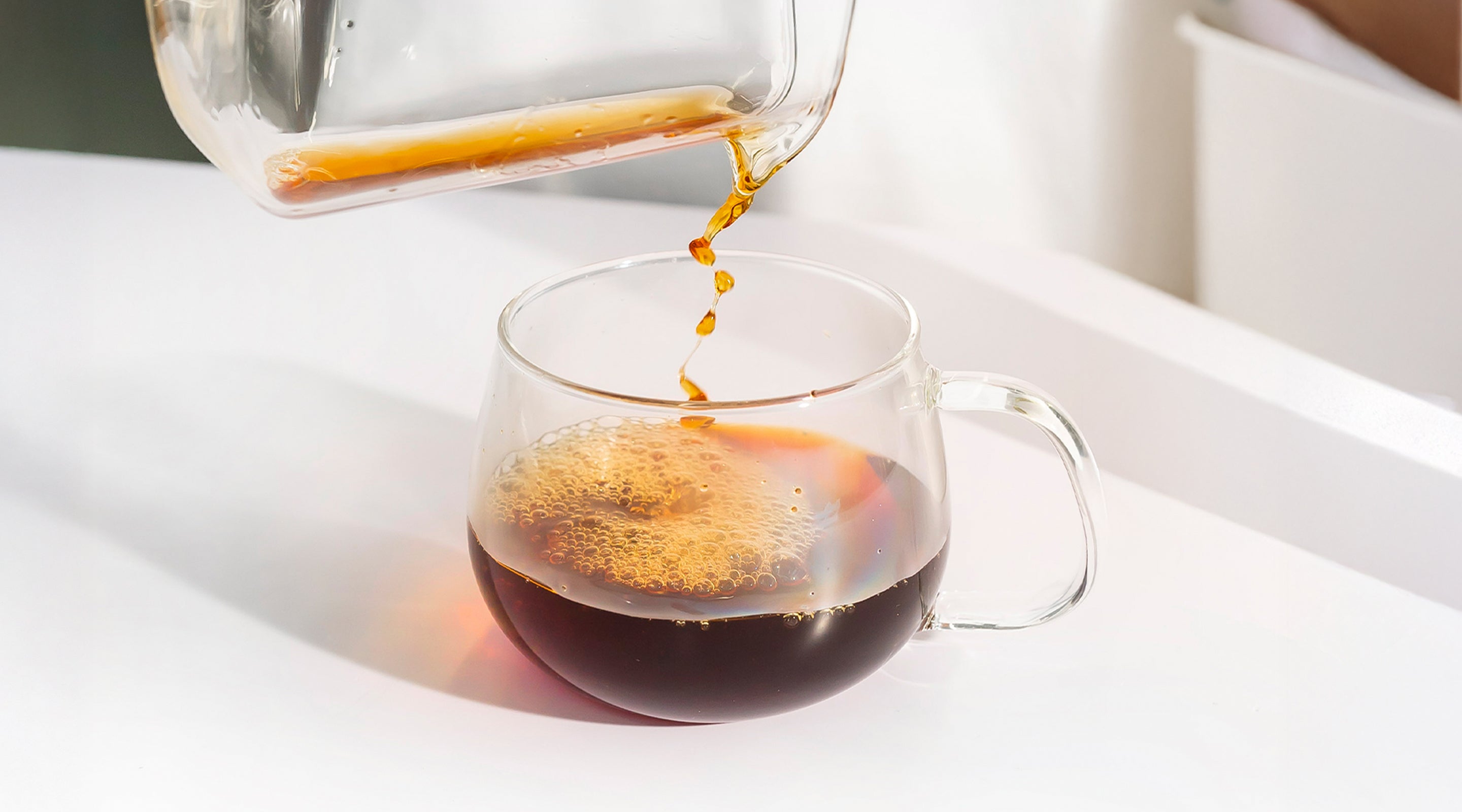 Industry Beans Filter Coffee being poured from a glass carafe into a clear glass mug on a white surface.