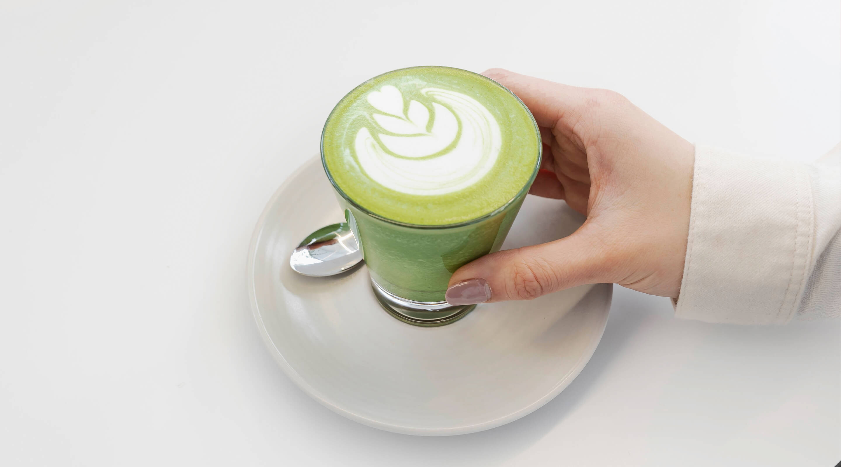 Hand holding a matcha latte with a white background