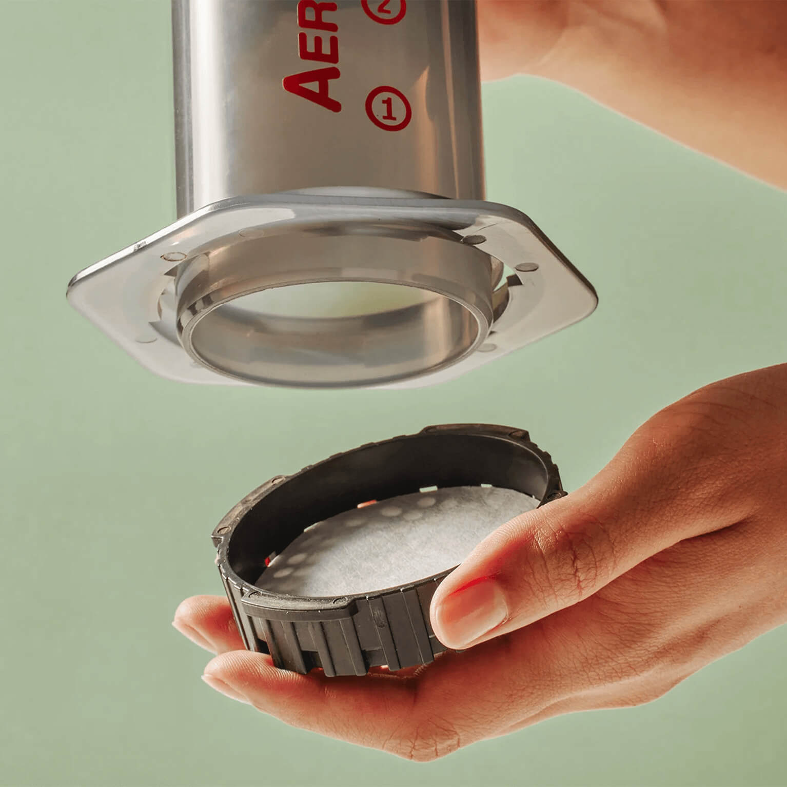 person's hand holding Clear Aeopress with Aeropress Paper Filters