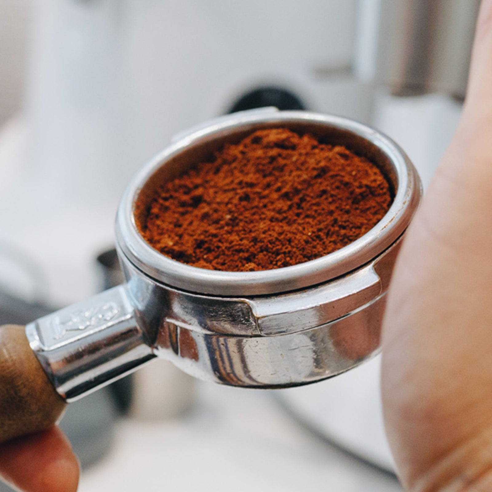 Hand holding a portafilter filled with ground coffee