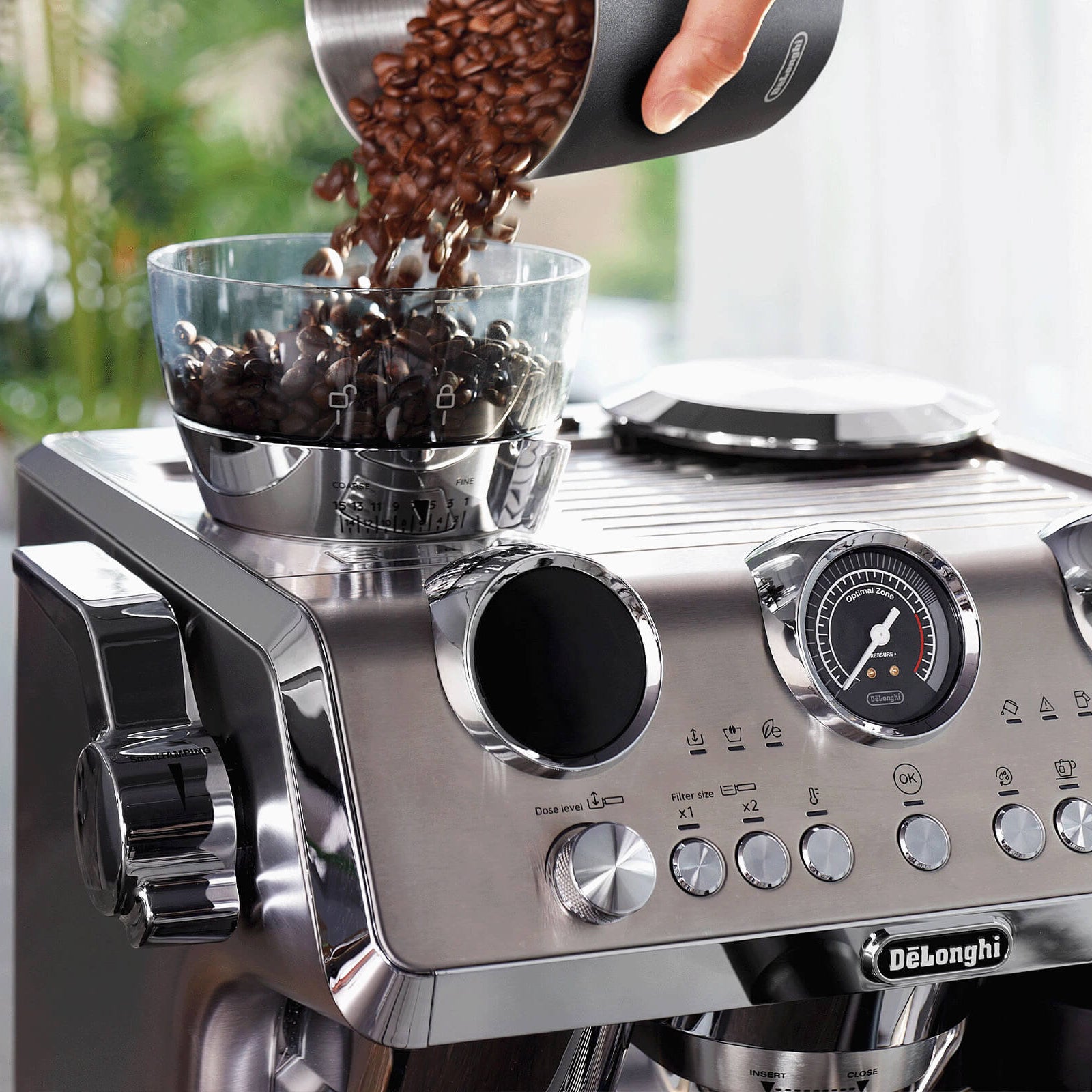 Espresso machine with coffee beans being poured into it on a kitchen counter.