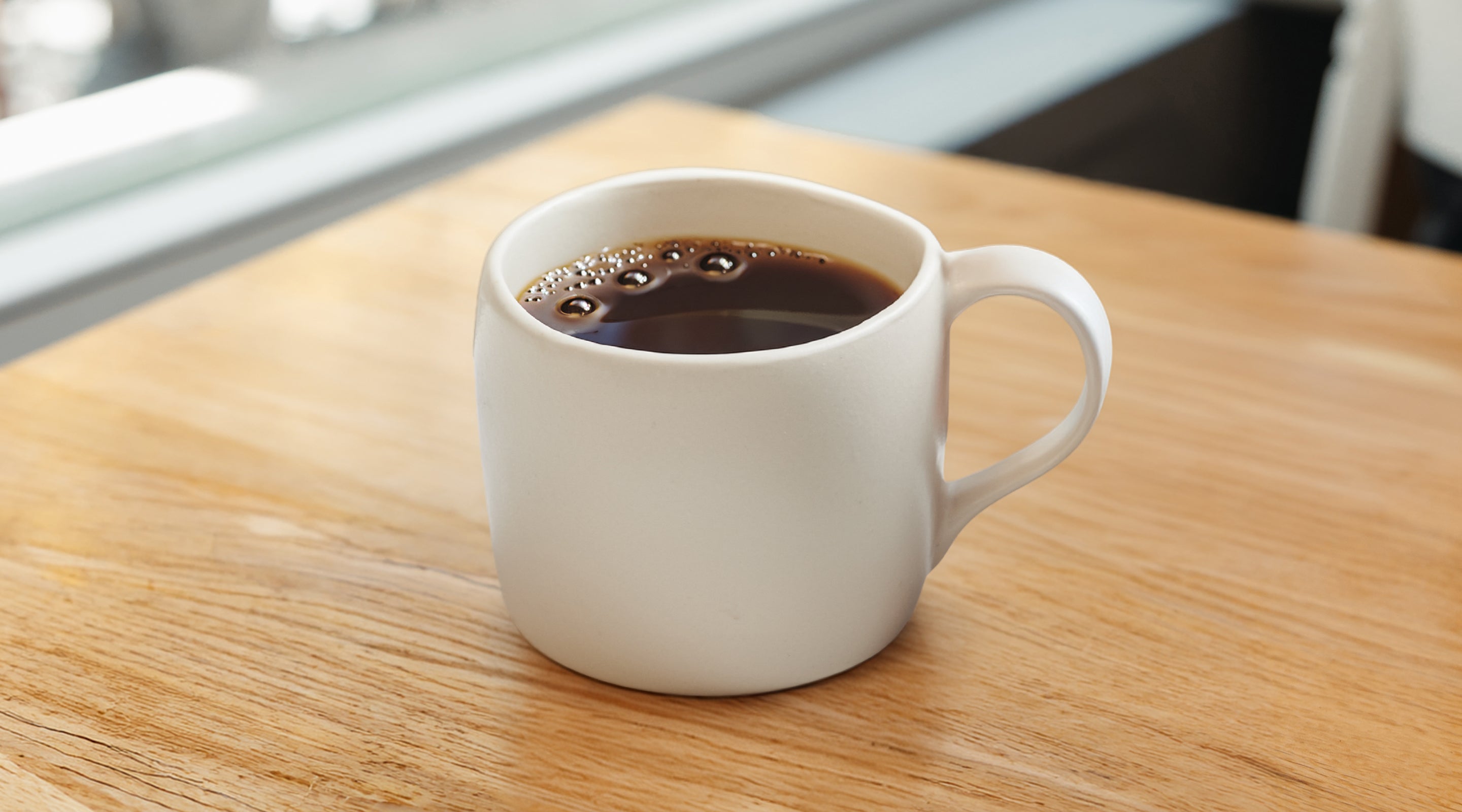 White ceramic mug on wooden table filled with Industry Beans filter single origin coffee