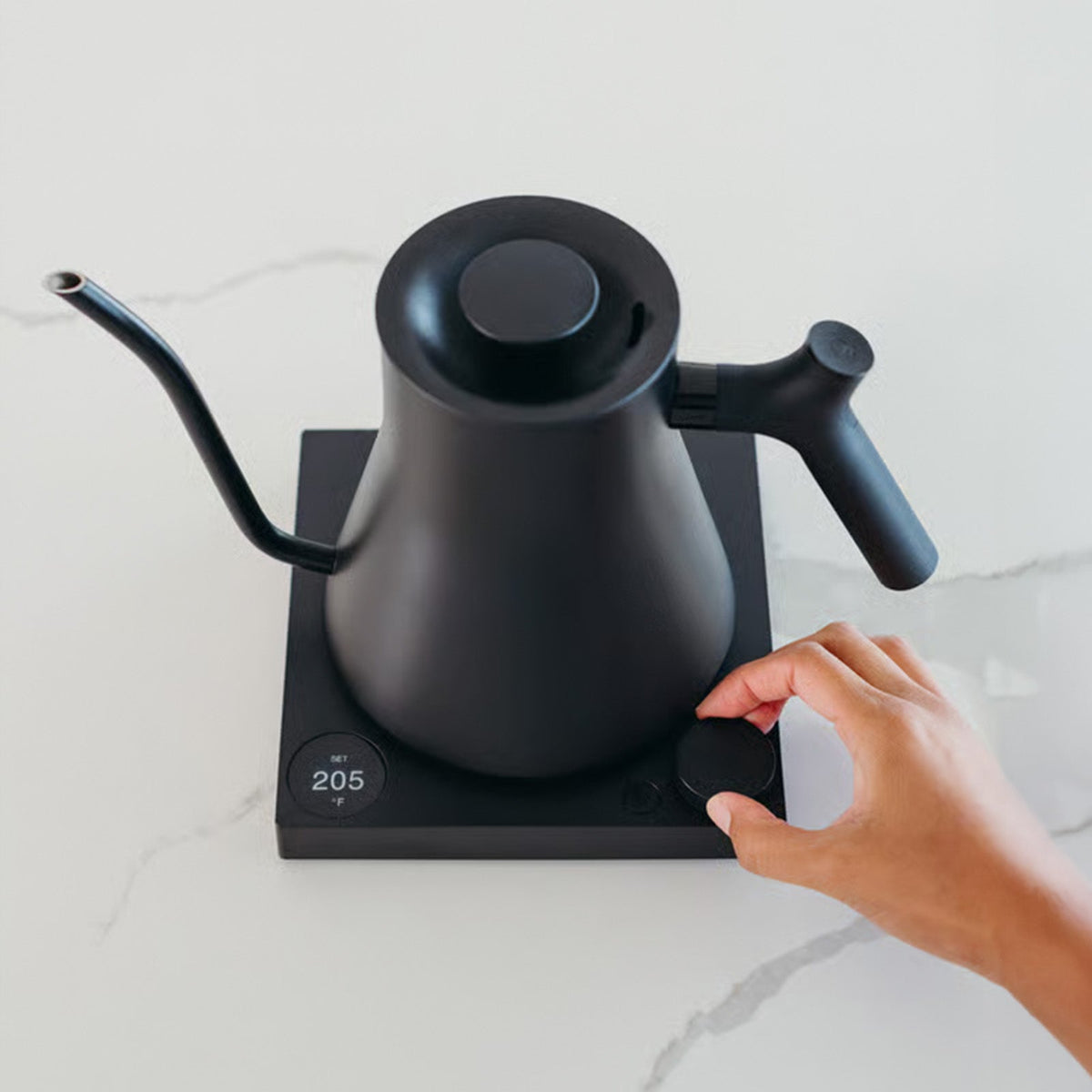 Matte Black Fellow Stagg EKG Pro Electric Kettle on white surface with hand adjusting the template control