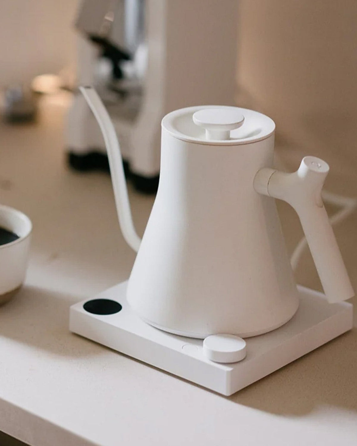 Matte White Fellow Stagg EKG Pro Electric Kettle on white bench with brewed filter coffee in a ceramic mug