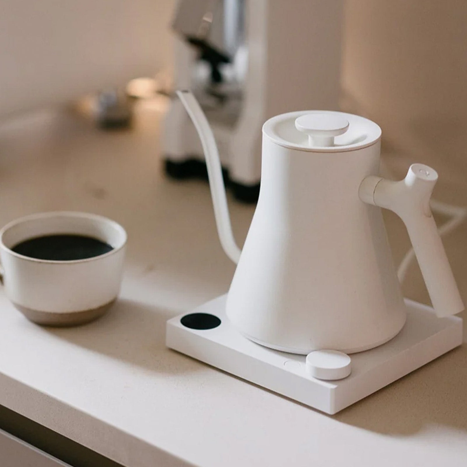 Matte White Fellow Stagg EKG Pro Electric Kettle on white bench with brewed filter coffee in a ceramic mug