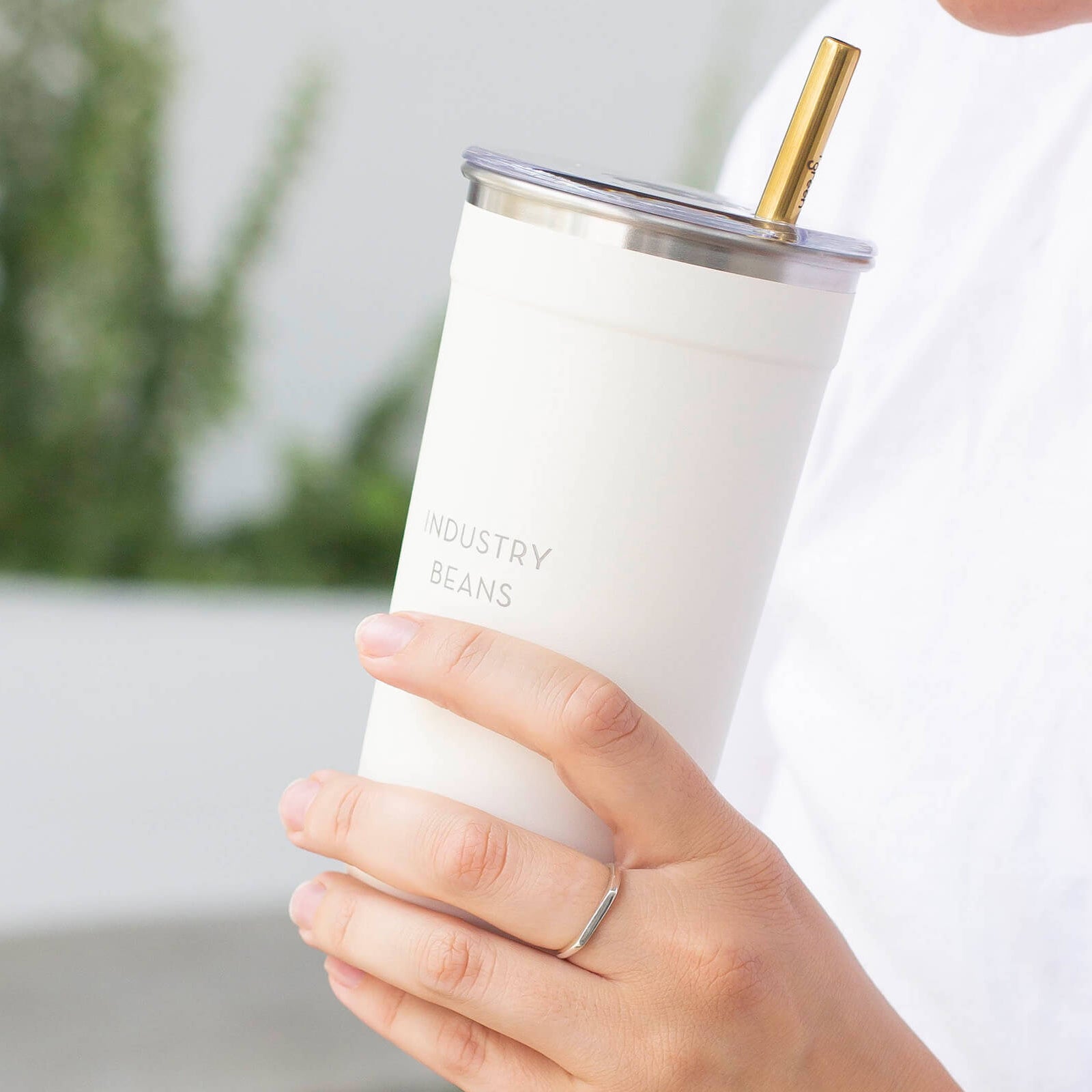 Person holding a white tumbler with a gold straw lid outdoors