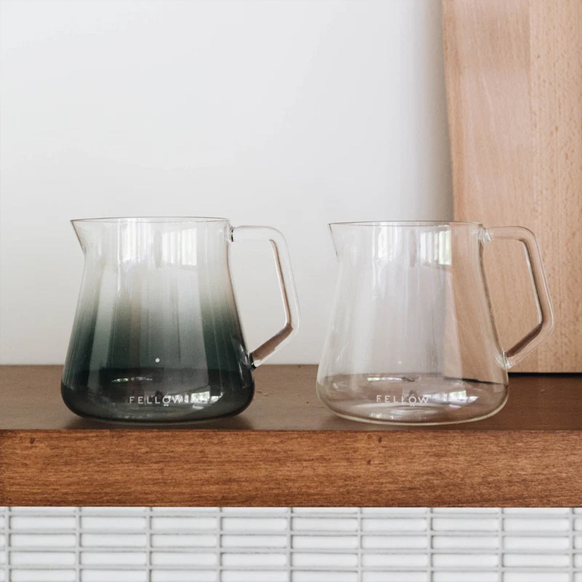 Fellow Mighty Small Glass Carafe in Smoke and Clear side by side on a timber shelf