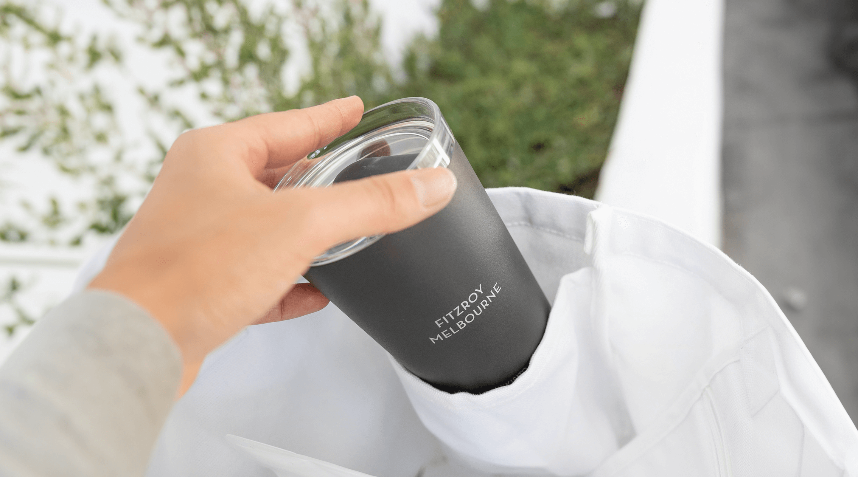 Hand pulling reusable coffee cup out of bag