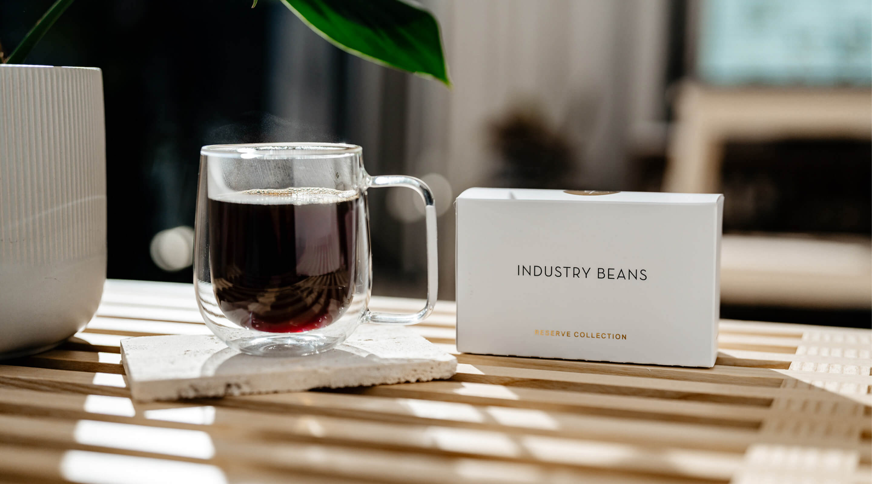 Clear glass mug with dark liquid on a table next to a box labeled 'Industry Beans'.