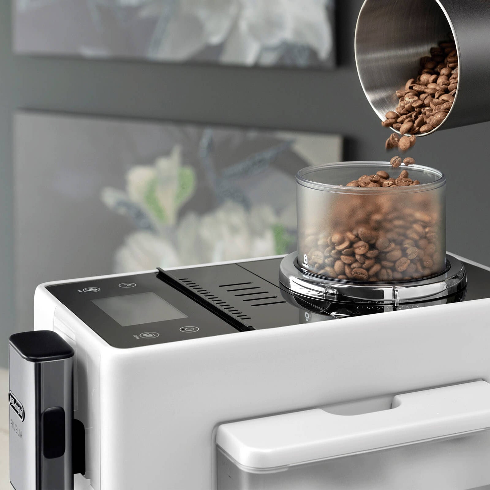 Coffee grinder with coffee beans being poured into it, set against a blurred indoor background.