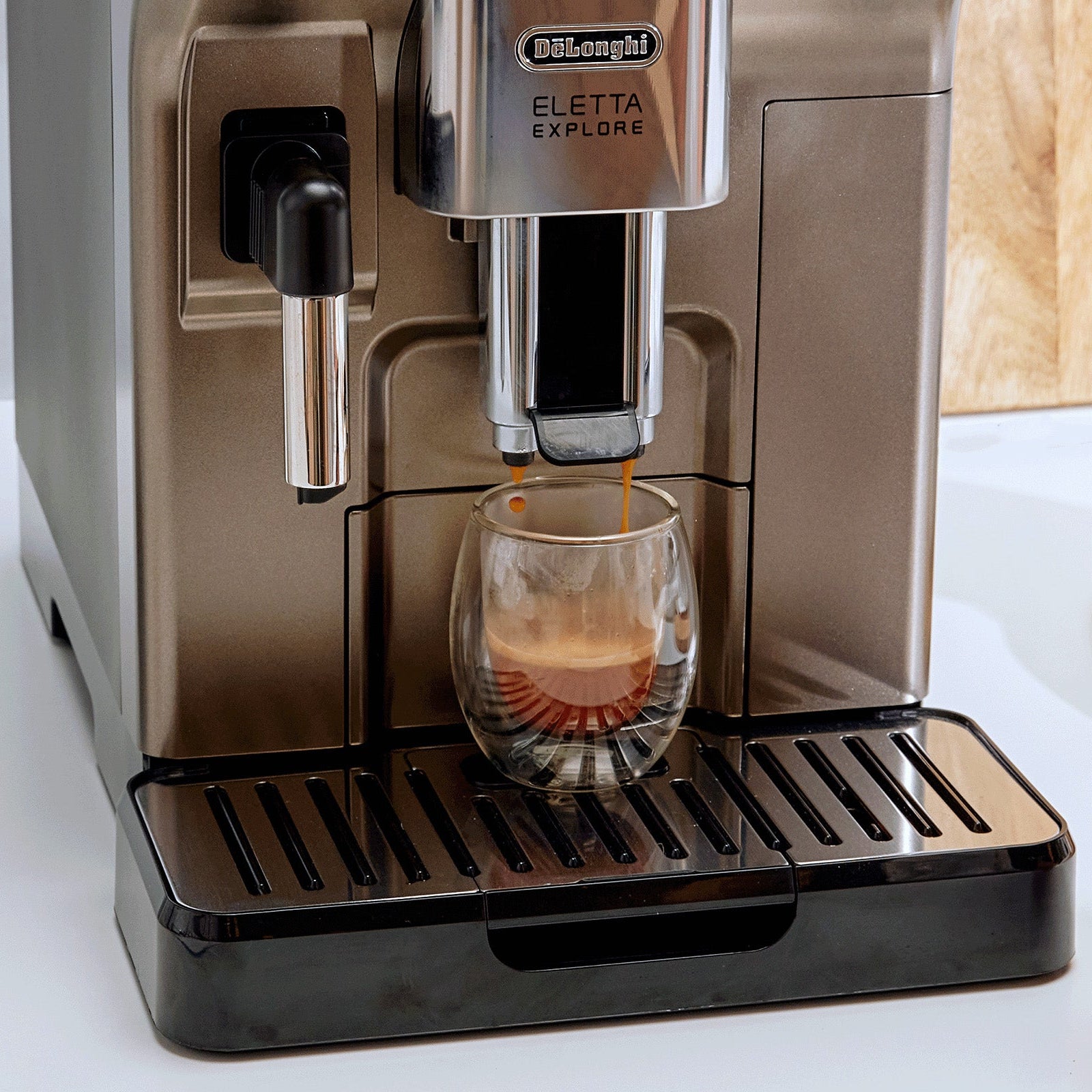 De'Longhi coffee machine dispensing coffee into a glass with a hand holding a smartphone nearby.
